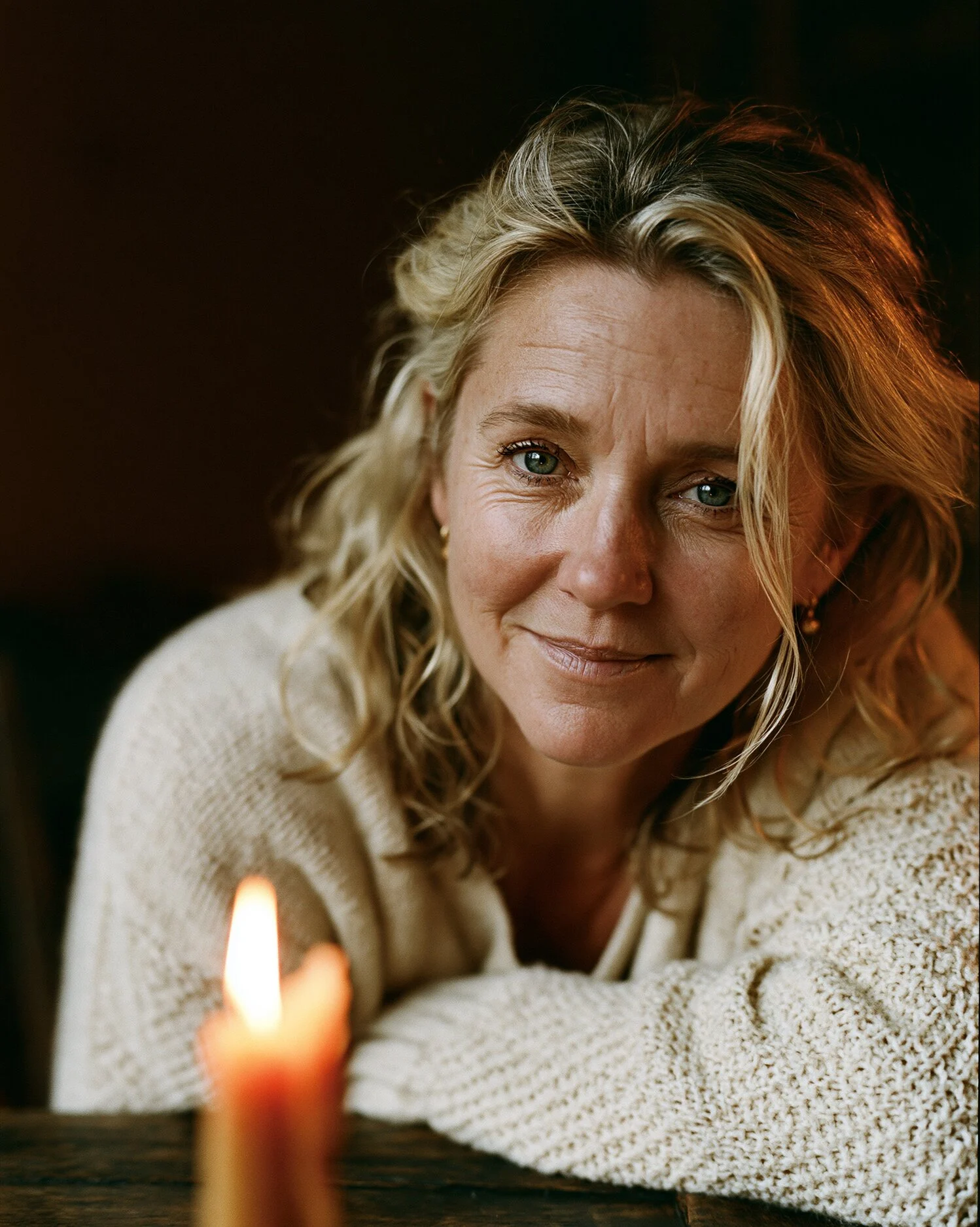 Vesper, Brooklyn tarot reader, smiling softly by candlelight at her reading table — warm portrait for Tarot of the Boroughs